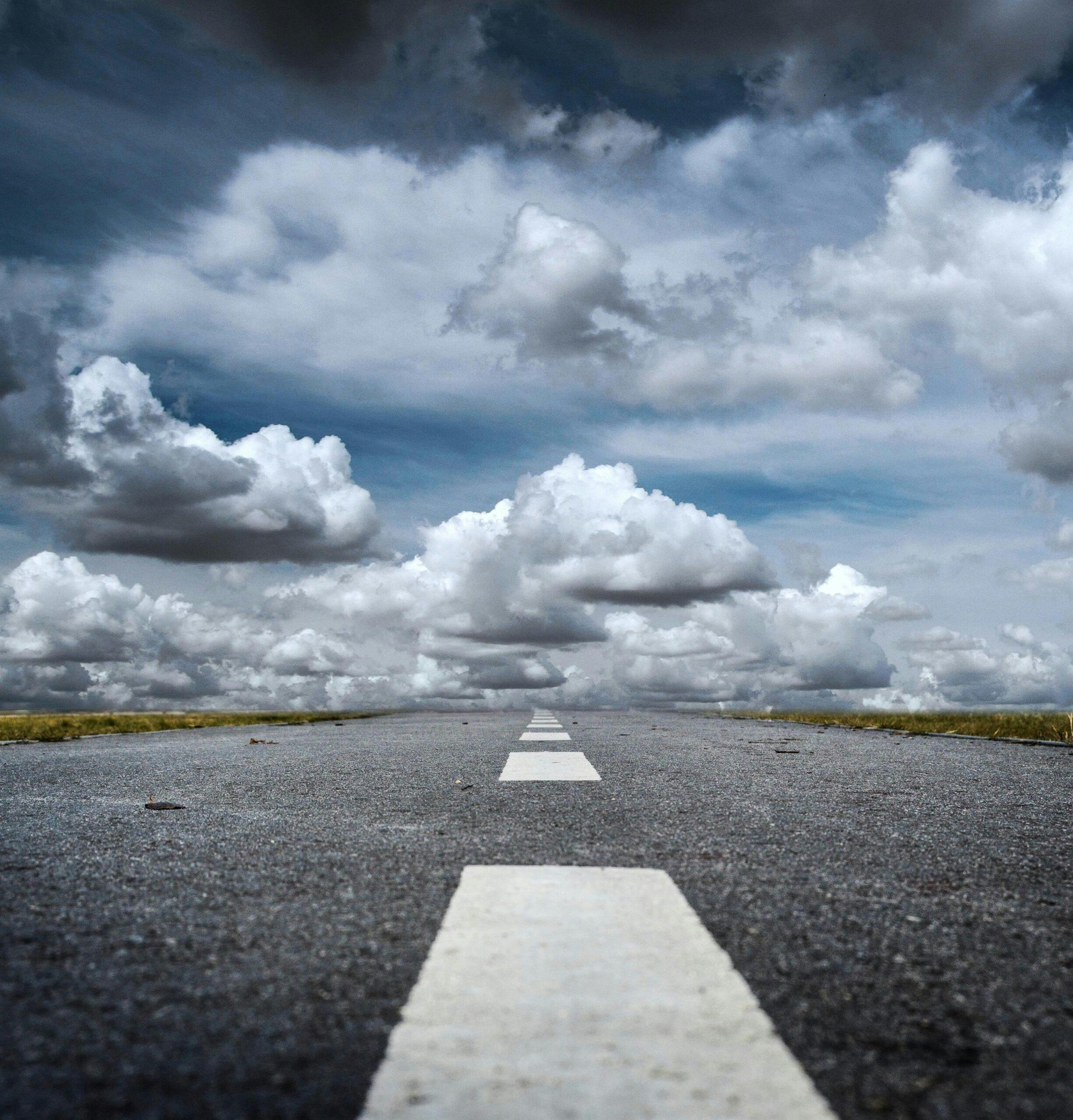 A straight road stretched toward a dramatic sky filled with fluffy clouds, creating a sense of journey.